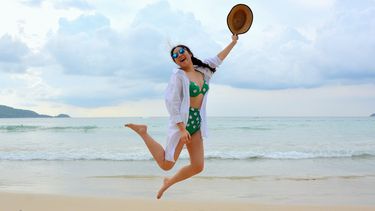 vrouw met hoed springt op het strand en voelt zich zelfverzekerd in zwemkleding