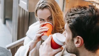 Vrouw die de man aankijkt tijdens hun date terwijl ze koffie drinkt, omdat ze benieuwd is wat de man het eerst aan haar opvalt
