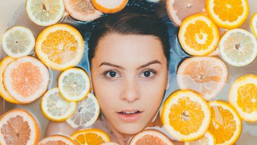 Gezicht van vrouw omringt door citroenen en grapefruit: Vitamine C voor je huid