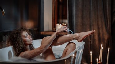 Vrouw die probeert haar benen glad te scheren in bad