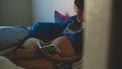 Vrouw met zwangere buik leest boekje en denkt aan babynaam