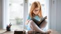 Roodharig meisje zit met een grote bril in kleermakerszit een boekje te lezen: een van de goede gewoonten die een kind kan aanleren