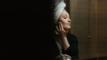 Vrouw die in de spiegel haar gezichtsverzorging doet omdat ze last heeft van droge en gevoelige huid en acné door haar mondmasker