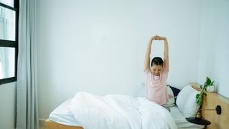 Vrouw rekt zich uit in bed, en voelt de voordelen van een ochtendroutine