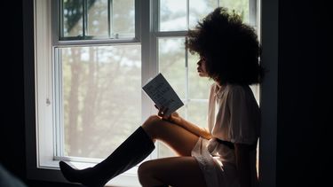 Vrouw zit op vensterbank te lezen en is eenzaam