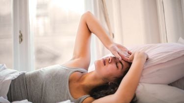 Vrouw ligt op bed en voelt aan haar hoofd, wat kan betekenen dat ze een opvlieger heeft: een van de tekenen van pre menopauze