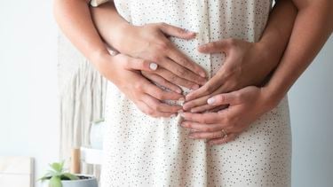 Vrouw die haar handen en de handen van haar partner op haar buik heeft omdat ze tijdens de zwangerschap toch een missed abortion heeft