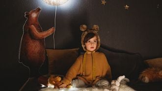 Kind dat rond bedtijd op bed zit in ee berenpyjama, klaar om te slapen