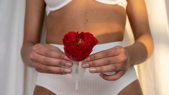 menstruatie na bevalling / vrouw houdt rode bloem en menstruatiecup voor vagina