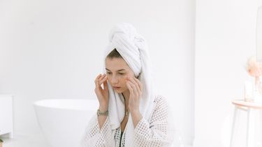 Vrouw in witte badjas en handdoek op haar hoofd brengt zalf aan op haar gezicht. Skincare in de koelkast