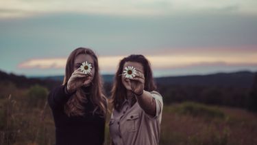 twee vrouwen staan in een weide met een bloem in de hand