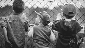 Drie jongens die door een hek staan kijken