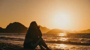 Vrouw zit op strand met zonsondergang en heeft spijt
