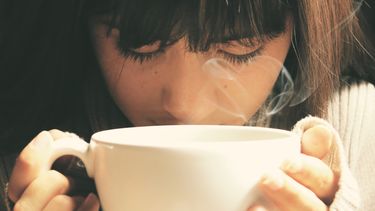 Vrouw die aan een kop koffie ruikt en wil afvallen