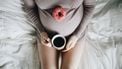 vrouw die met een kopje koffie en een donut op haar zwangere buik zit te genieten