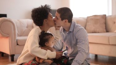 Twee partners die samen een kind opvoeden en elkaar een kus geven