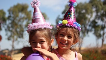 Twee meisjes met feestmutsen op en een ballon die een kinderfeestje vieren