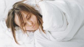 Vrouw die in bed ligt in de dekens gewikkeld omdat ze het koud heeft