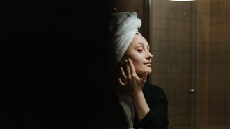Vrouw die in de spiegel haar gezichtsverzorging doet omdat ze last heeft van droge en gevoelige huid en acné door haar mondmasker