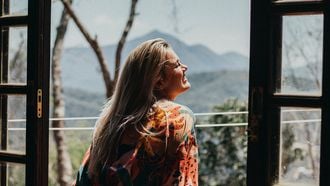 meisje kijkt uit het raam en lacht vrolijk omdat ze van zichzelf houdt