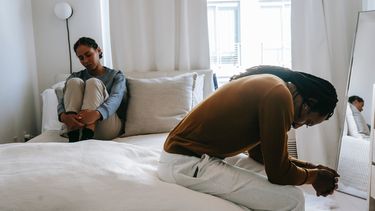 Vrouw die in haar relatie te maken heeft met gaslighting door een narcist en ongelukkig op bed zit terwijl de man teleurgesteld kijkt