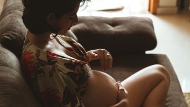Vrouw die op de bank zit en zichzelf een zwangerschapsmassage geeft