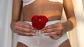 menstruatie na bevalling / vrouw houdt rode bloem en menstruatiecup voor vagina