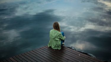 Vrouw die op een stijger naar het water kijkt en zich eenzaam en gebroken voelt