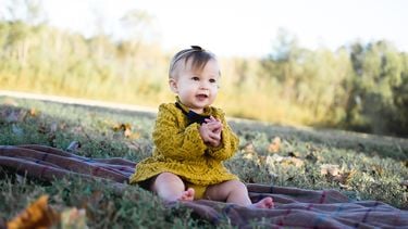 Een oktober kindje dat buiten op een kleedje zit in de herfst