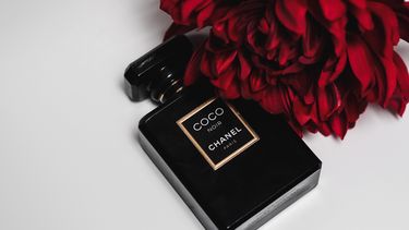 Zwart parfumflesje Coco Chanel met rode roos. Lessen van coco chanel