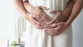 Vrouw die haar handen en de handen van haar partner op haar buik heeft omdat ze tijdens de zwangerschap toch een missed abortion heeft