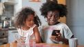 Vrouw die haar dochter op schoot heeft en op haar telefoon kijkt