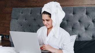 Vrouw zit met handdoek te achter haar laptop en heeft het thuiswerken onder de knie