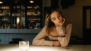 Vrouw die alleen aan de bar zit met een glas wijn en het heeft uitgemaakt met haar beste vriendin