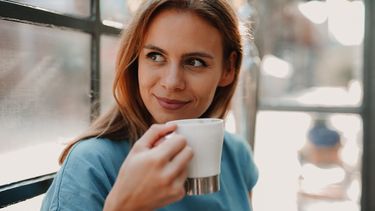 vrouw drinkt in haar eentje een kop koffie en is blij