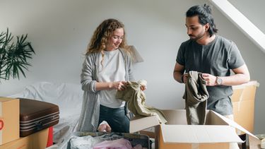 Man en vrouw pakken kleren in dozen en ontdekken de voordelen van wegdoen van kleren