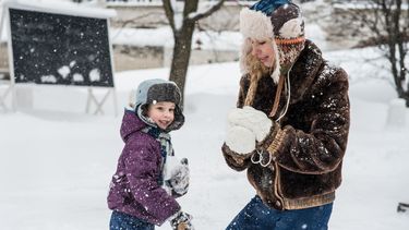 Jongensmoeder en haar zoon die sneeuwballen gooien in de sneeuw