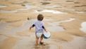 Peuter loopt op het strand om een emmertje water te halen