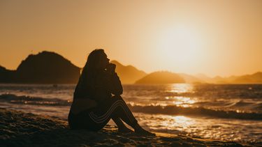 Vrouw zit op strand met zonsondergang en heeft spijt