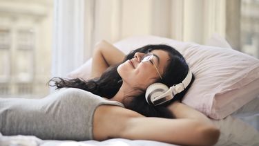 Vrouw met koptelefoon op in bed die naar een luisterboek luistert