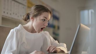 Vrouw die verrast is over de life hacks die ze op de laptop leest over het ouderschap