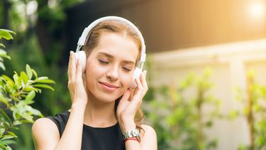 Vrouw met witte headphone lacht en luistert naar muziek, ze gebruikt muziek als therapie