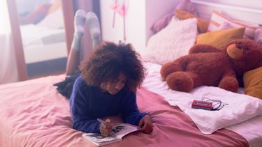 Meisje dat op haar bed ligt en in haar dagboek schrijft