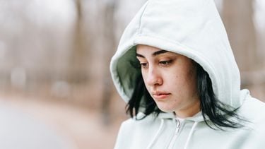 Vrouw met hoodie kijkt verdrietig omlaag, ze weet niet wat de oorzaken van haar onzekerheid zijn