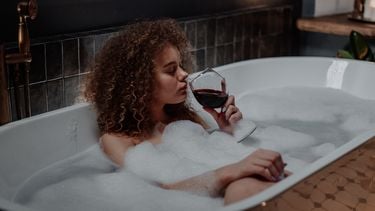 Vrouw in bad drinkt rode wijn. Verslaving
