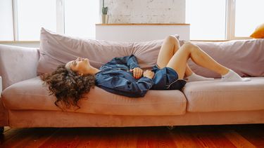 Vrouw die op de bank ligt en haar buik vasthoudt omdat ze zich slecht voelt door de pil