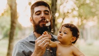 Man draagt zijn baby en blaast op bloem, hij is een van de type vaders